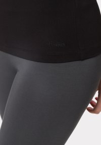 Schwarzes, tailliertes Oberteil mit dem Logo "LES LUNES" am Saum, kombiniert mit grauen Leggings. Beide Teile bestehen aus dehnbarem, glattem Material.