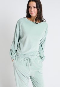 Ensemble de loungewear à rayures vert clair avec une coupe décontractée. Le haut présente un large décolleté, et le pantalon a une taille ajustable avec cordon.