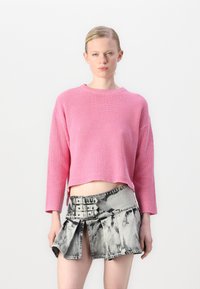 Maglione rosa a costine con un design cropped; abbinato a una minigonna in denim grigia con uno stile a pieghe e dettagli con fibbia.