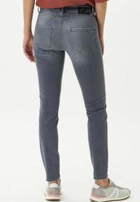 Jeans skinny grigi con vita media, tasche posteriori sottili e una texture denim liscia. Indossati con sneakers grigie e una maglietta rossa.