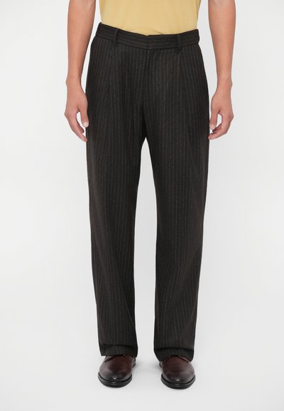 Pantalons noir à rayures fines en tissu lisse, présentant une coupe droite et une taille ajustée. Portés avec des chaussures marron.