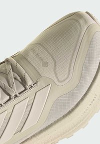 Light grey athletic shoe featuring a textured surface, geometric patterns, and supportive overlays. Includes reflective accents and a durable sole.