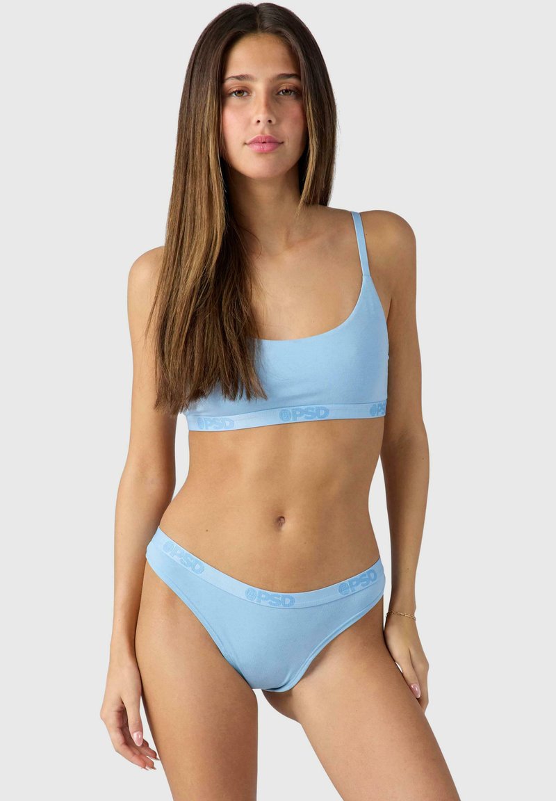 Light blue seamless bralette with thin straps and matching thong, featuring a band with logo, made from soft, stretchy fabric.