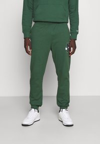 Gröna joggerbyxor i mjukt material, med resårmidja, avsmalnande ben och en svart Nike-logga på vänster lår.