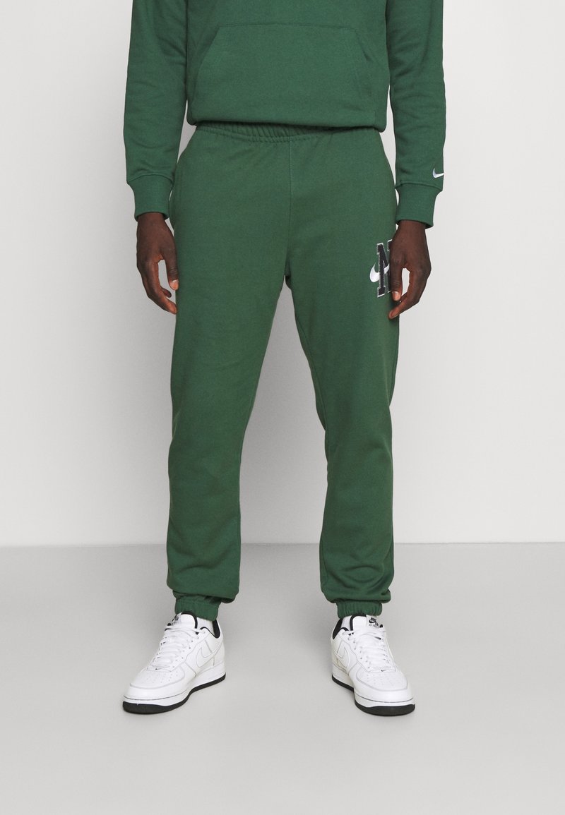Gröna joggerbyxor i mjukt material, med resårmidja, avsmalnande ben och en svart Nike-logga på vänster lår.