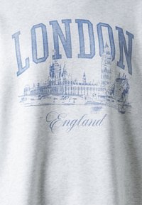 Sudadera gris con un gráfico azul del horizonte de Londres, con el texto "LONDON" y "England" abajo. Textura suave y diseño casual.