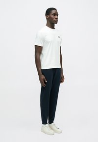 Fehér rövid ujjú póló kis fekete logóval, tengerészkék melegítőnadrággal és világos színű tornacipővel párosítva.