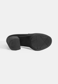 Zwarte hoge hak met een gestructureerde rubberen zool en een vierkante hak. De zool heeft gekruiste lijnen voor grip en stabiliteit. Gladde bovenzijde.