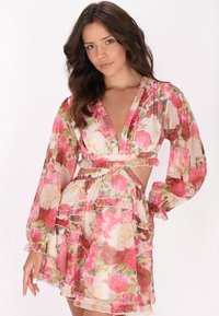 Rochie florală cu mâneci lungi, decolteu adânc �în formă de V, accente volanate și detalii decupate. Fabricată dintr-un material subțire și ușor în nuanțe de roz și crem.