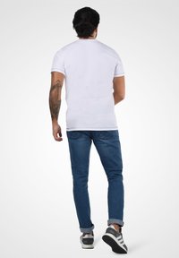 Bela bombažna majica s krojem okrog vratu, kratkimi rokavi, v kombinaciji z modrimi jeans hlačami, ki kažejo sproščen kroj in zavihane manšete.