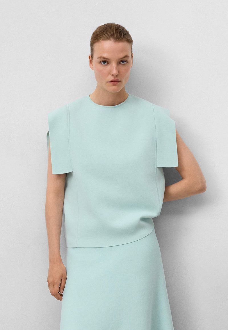 Jasnoniebieski, strukturalny top z szerokimi akcentami na ramionach i okrągłym dekoltem. Gładki, teksturowany materiał przechodzi w pasującą spódnicę.