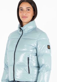 Lichtblauwe pufferjack met een glanzende afwerking, hoge kraag en ritszakken. Bevat zwarte hardware en een embleem op de mouw.