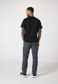 Sort bomulds T-shirt parret med grå cargo bukser, der har sidelommer og elastiske cuffs. Båret med sorte og hvide sneakers.