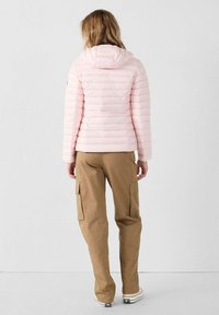 Lichtroze donsjack met horizontale stikdetails, een capuchon en een slanke pasvorm, gecombineerd met beige cargobroek en witte sneakers.