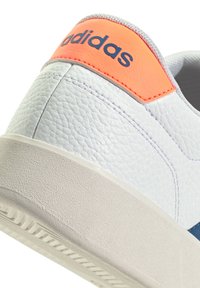 White textured leather sneaker with a light gray sole, featuring a bright orange accent on the heel and navy branding.