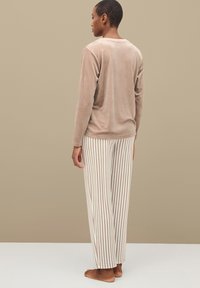 Top de terciopelo de manga larga en color beige claro. Pantalones de pijama de corte relajado en rayas beige y crema. Diseño simple, textura suave y sin herrajes visibles.