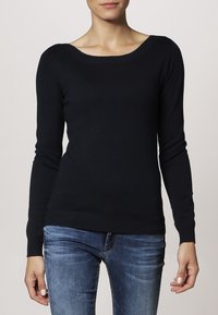 Marineblauer Strickpullover mit weitem Ausschnitt, langen Ärmeln und gerippten Säumen. In Kombination mit blauen Jeans wirkt der Stoff weich und glatt.
