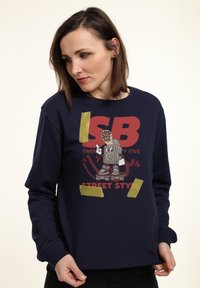 Felpa blu navy con stampa grafica di un personaggio dei cartoni animati su uno skateboard, con il testo "ISB TWENTY FIVE" e "STREET STYLE".