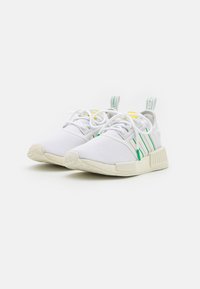 Zapatillas deportivas blancas con acentos en verde y amarillo, parte superior de malla, lengüeta acolchada y suela texturizada. Presenta pestañas para tirar en los talones.