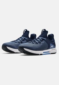 Blå nätidrottsskor med svarta gummisulor, med en vit mellansula och blå detaljer. Snörningsdesign med dragflikar på hälarna.