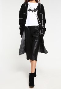 Svart stickad cardigan med vita ränder över en vit t-shirt med en fladdermusdesign, i kombination med svarta läderculottes och ankelskor.