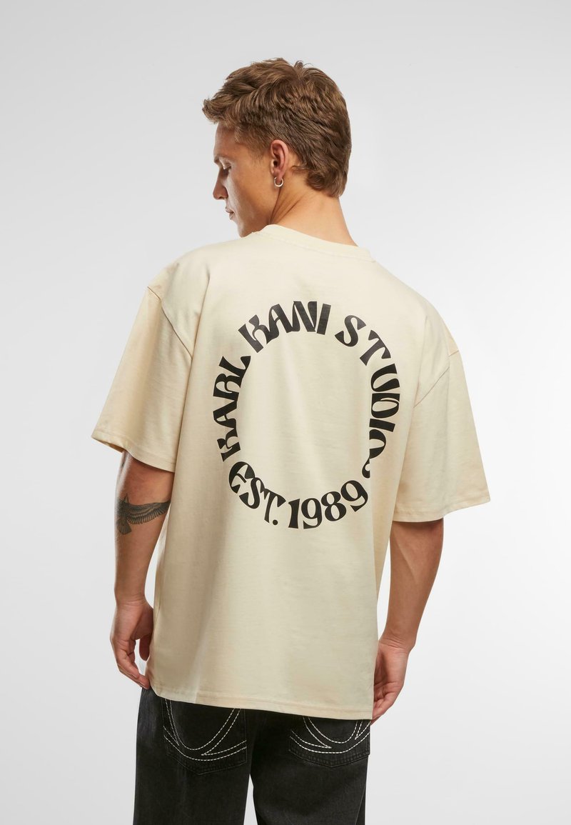Šviesiai ruda, per didelė medvilninė marškinė, su juodu apvaliu logotipu ir inscription "BRAND KANI STUDIO EST. 1989" ant nugaros. Trumpomis rankovėmis.