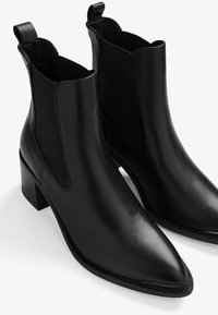 Paire de bottines en cuir noir avec bouts pointus, talons blocs et panneaux latéraux élastiques.