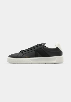 Zapatilla negra de cuero con suela de goma blanca. Presenta cordones negros y un diseño minimalista. Logo dorado de ARKK en el lateral.