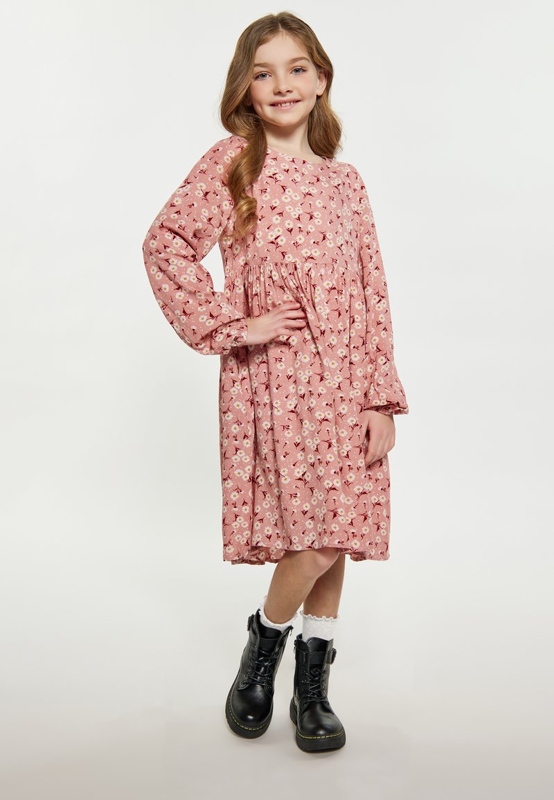 Roze bloemenjurk met lange mouwen, geplooid middel en een knie-lange zoom, gecombineerd met zwarte veterschoenen en witte kanten sokken.