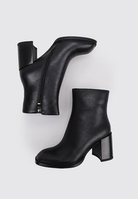 Botines negros de cuero suave con un tacón geométrico y cierre de cremallera lateral. Forma elegante y ajustada con acabado mate.