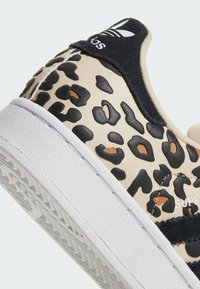 Baskets Adidas avec imprimé léopard beige et noir, semelle blanche, languette de talon noire avec logo Adidas et texte "SUPER" sur le côté.
