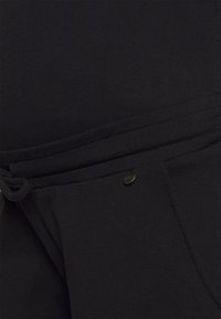 Calças jogger em mistura de algodão pretas, com cordão ajustável e um pequeno logótipo metálico na frente do bolso. Textura suave e design casual.