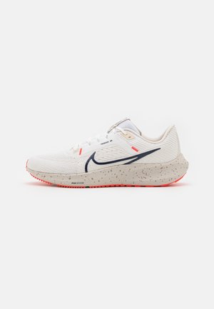 Nike Pegasus 40 Schuhe mit einem weißen Strick-Obermaterial, einem marineblauen Swoosh, einer beige gesprenkelten Mittelsohle und einer leuchtend roten Gummiaußensohle.