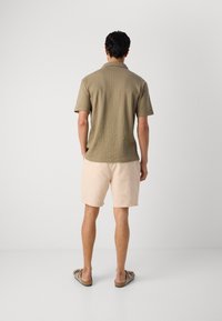 Kortærmet skjorte i olivengrøn med et struktureret mønster, parret med lysebeige shorts og brune slidssandaler.