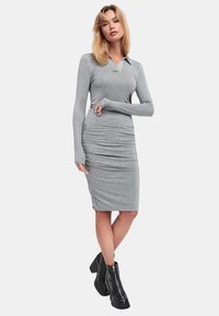 Abito lungo grigio a maniche lunghe con colletto, caratterizzato da un motivo testurizzato e dettagli arricciati in vita, abbinato a stivali neri alla caviglia.