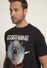 Sort bomulds t-shirt med et farverigt grafisk motiv af et skrigende ansigt omgivet af splinter, samt ordet "SCORPIONS" i fede, strukturerede bogstaver.