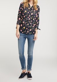 Camisa de botones de flores de manga larga, en azul marino con flores rosas y amarillas, combinada con jeans ajustados azul claro y zapatillas marinas.
