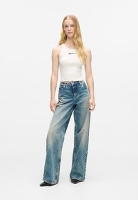 Balta ribota bez piedurknēm ar logo, apvienota ar gaiši ziliem platām kājām džinsiem ar izbalējušu efektu un sudraba detaļām. Melni apavi.