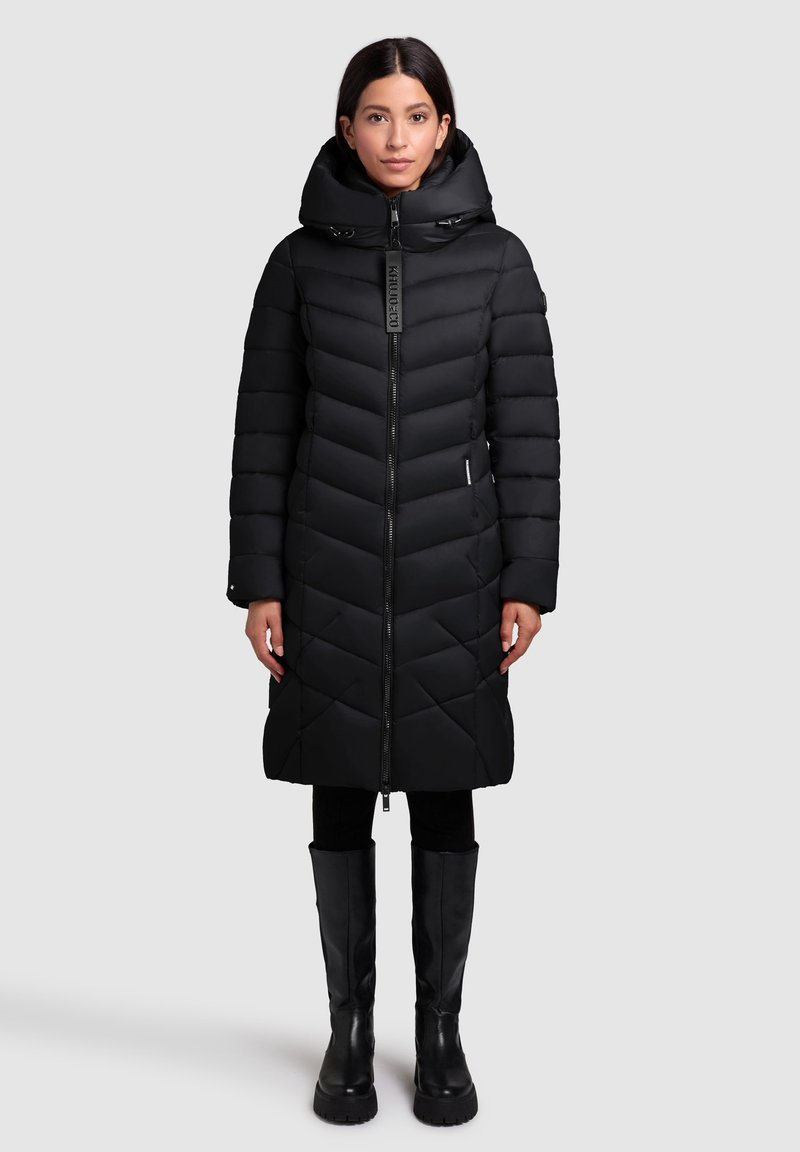 Black puffer coat with a quilted design, high collar, front zipper, and side pockets. Worn with black leggings and knee-high boots.