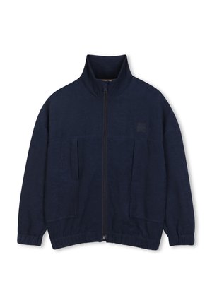 Marineblauwe jas met ritssluiting, hoge kraag, elastische manchetten en twee voorzakken, plat liggend op een witte achtergrond.