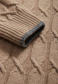 Sweter w nadruk łańcuszkowym w jasnobrązowym kolorze z prążkowanymi mankietami. Mankiety mają szary akcent. Fakturalny wzór na całej tkaninie dodaje głębi.
