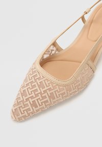 Beige kengännokka-slingback-kengät, joissa on kangasylä ja teksturoitu pinta sekä sileä beige nahkaremmi. Kevyesti pehmustettu ruskea sisäpohja.