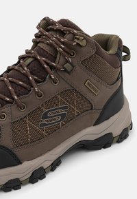 Botas de senderismo impermeables en marrón, con parte superior de malla y ante, acentos texturizados, cordones robustos y suela de goma resistente con profundos surcos.