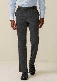 Pantalons gris ajustés en tissu texturé, avec une coupe droite et un devant plat. Des chaussures noires complètent la tenue.
