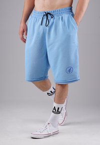 Light blue athletic shorts with an elastic waistband, side pockets, and a logo detail on the hem, paired with white socks and shoes.
