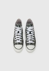 Vysoké tenisky so vzorom čierno-bielej zebry, biele šnúrky a biele gumové špičky, vystavené vedľa seba na bielom pozadí.