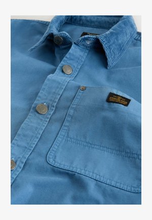 Mėlyna medvilninė maršina su sagomis. Yra veliūrinis apykaklė, metalinės užsegamos sagos ir krūtinės kišenė su prekės ženklo etikete. Minkšta tekstūra.