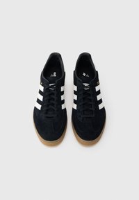 Black suede sneakers featuring three white stripes, a rubber gum sole, and a black lace-up design with minimal accents.