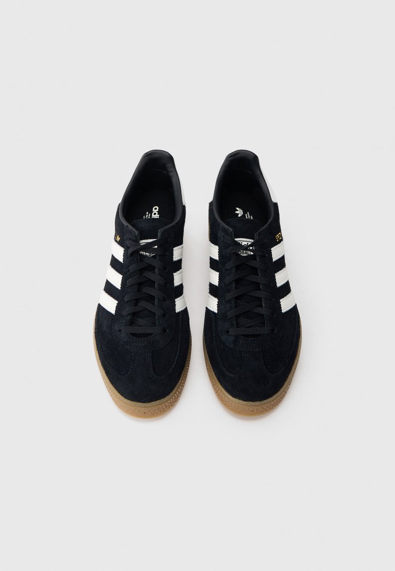 Black suede sneakers featuring three white stripes, a rubber gum sole, and a black lace-up design with minimal accents.