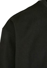 Black sweater with a ribbed texture, showing part of the shoulder and neckline. The fabric appears soft and stretches slightly.